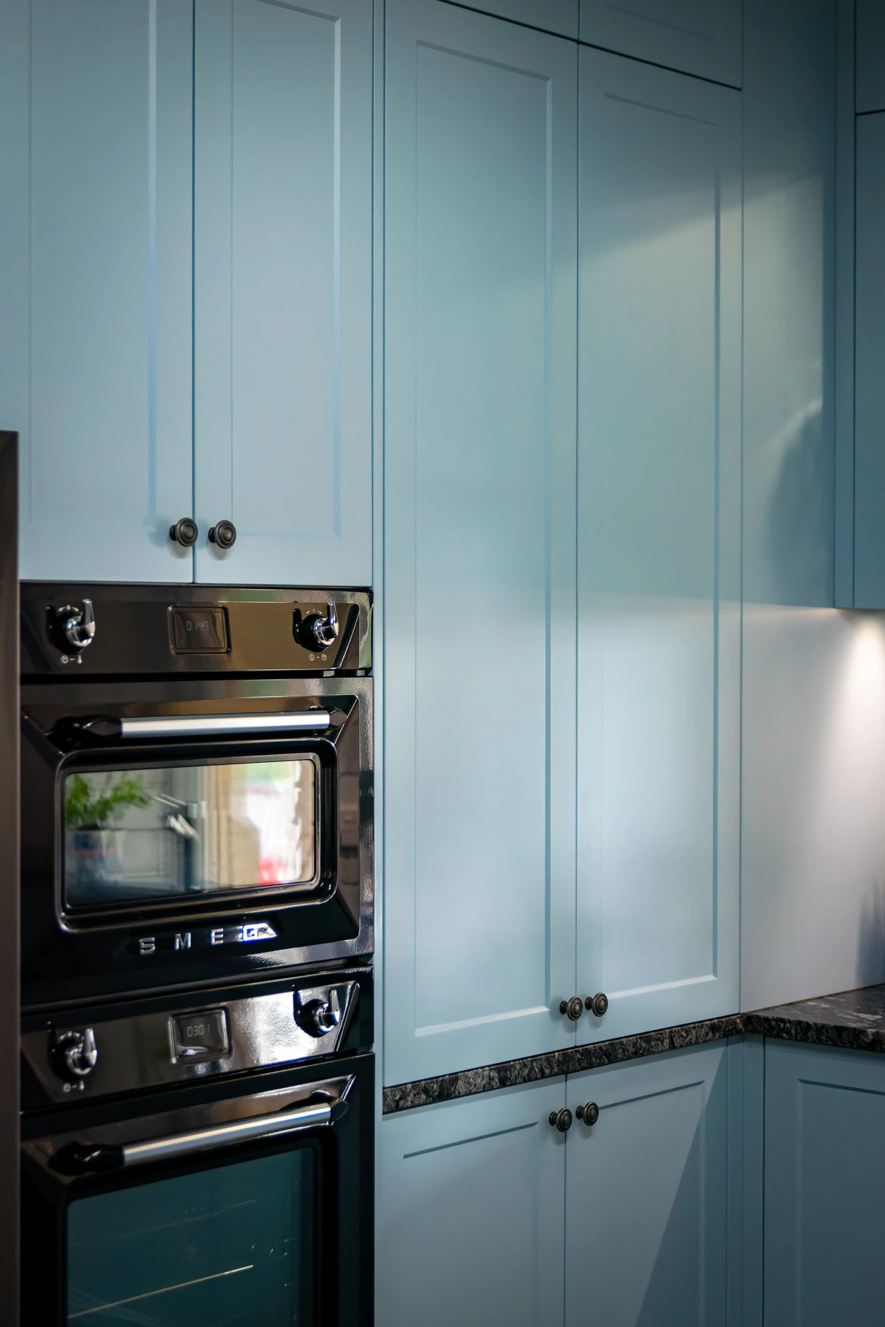 Modern Kitchen With Light Blue Cabinets, Black Oven, And Dark Marble Countertops.