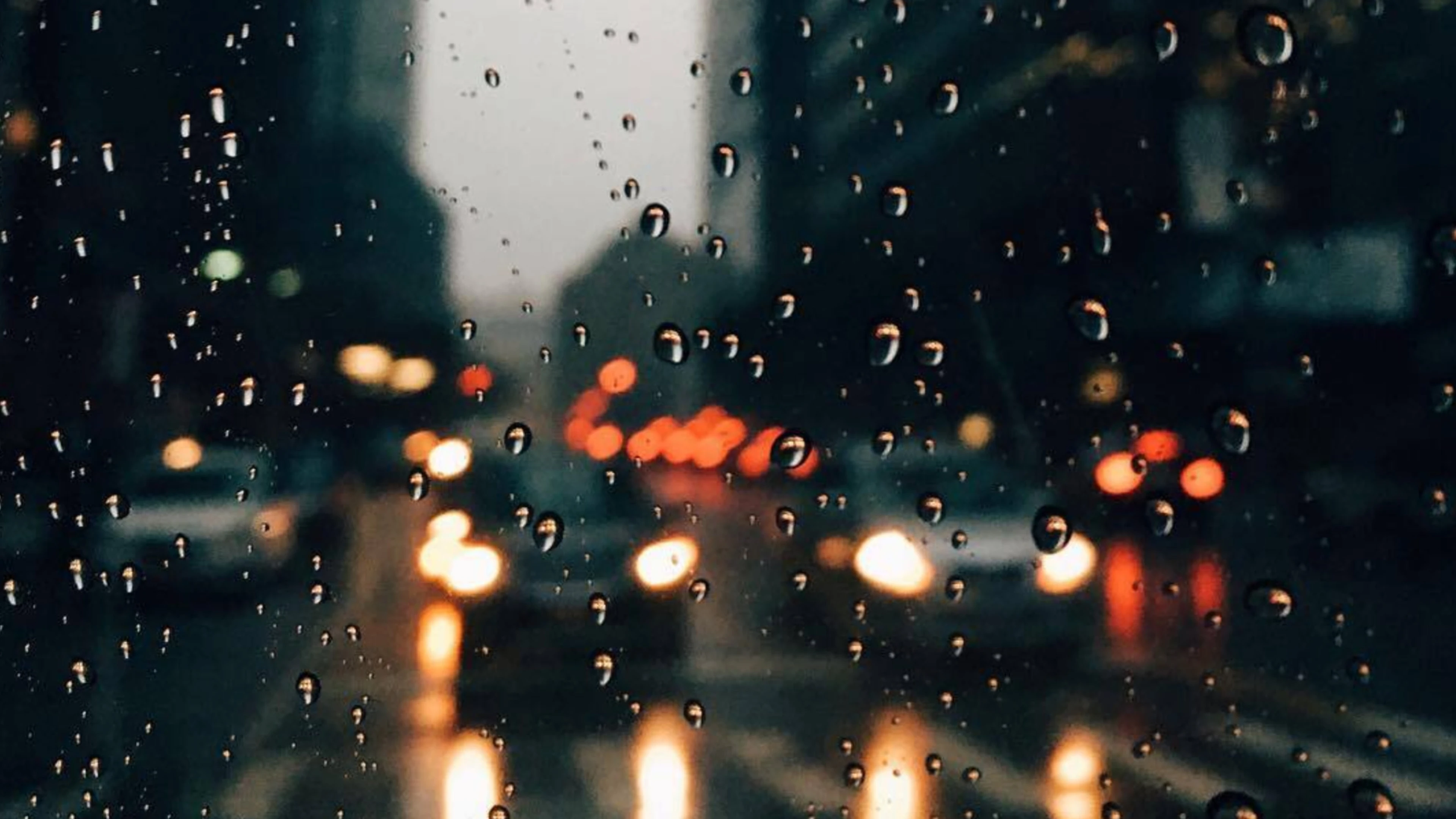Raindrops on window with blurred city lights and traffic, suggesting a rainy urban scene.