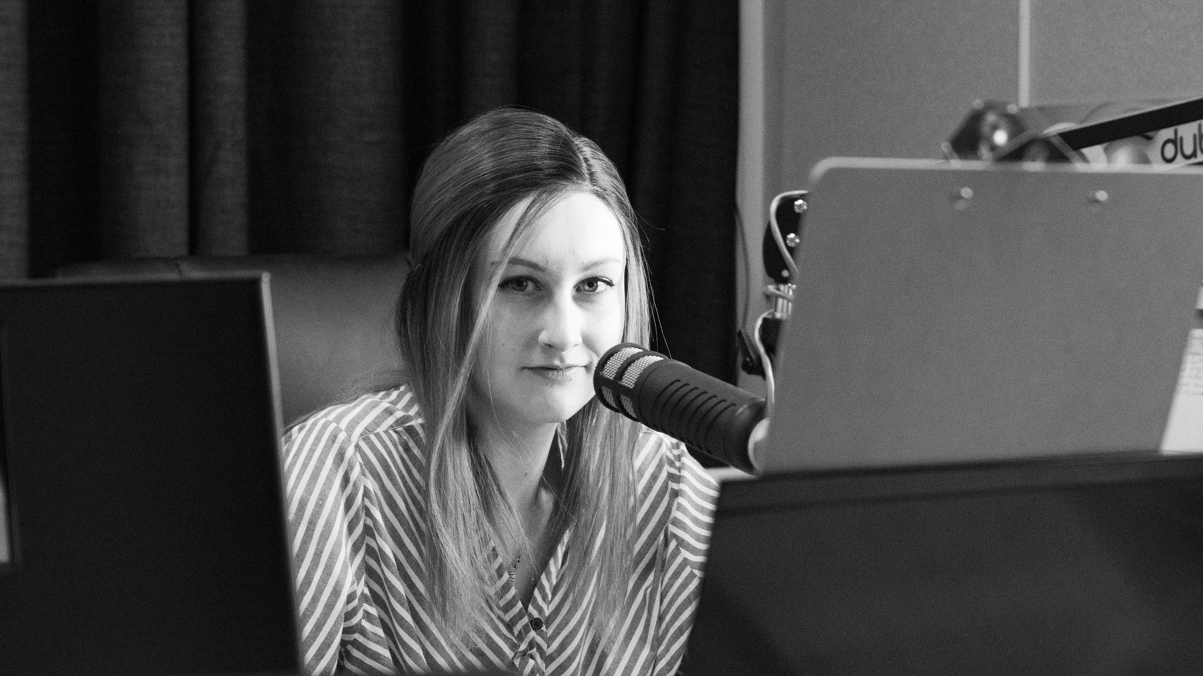 Person speaking into a microphone in a professional recording studio setup.