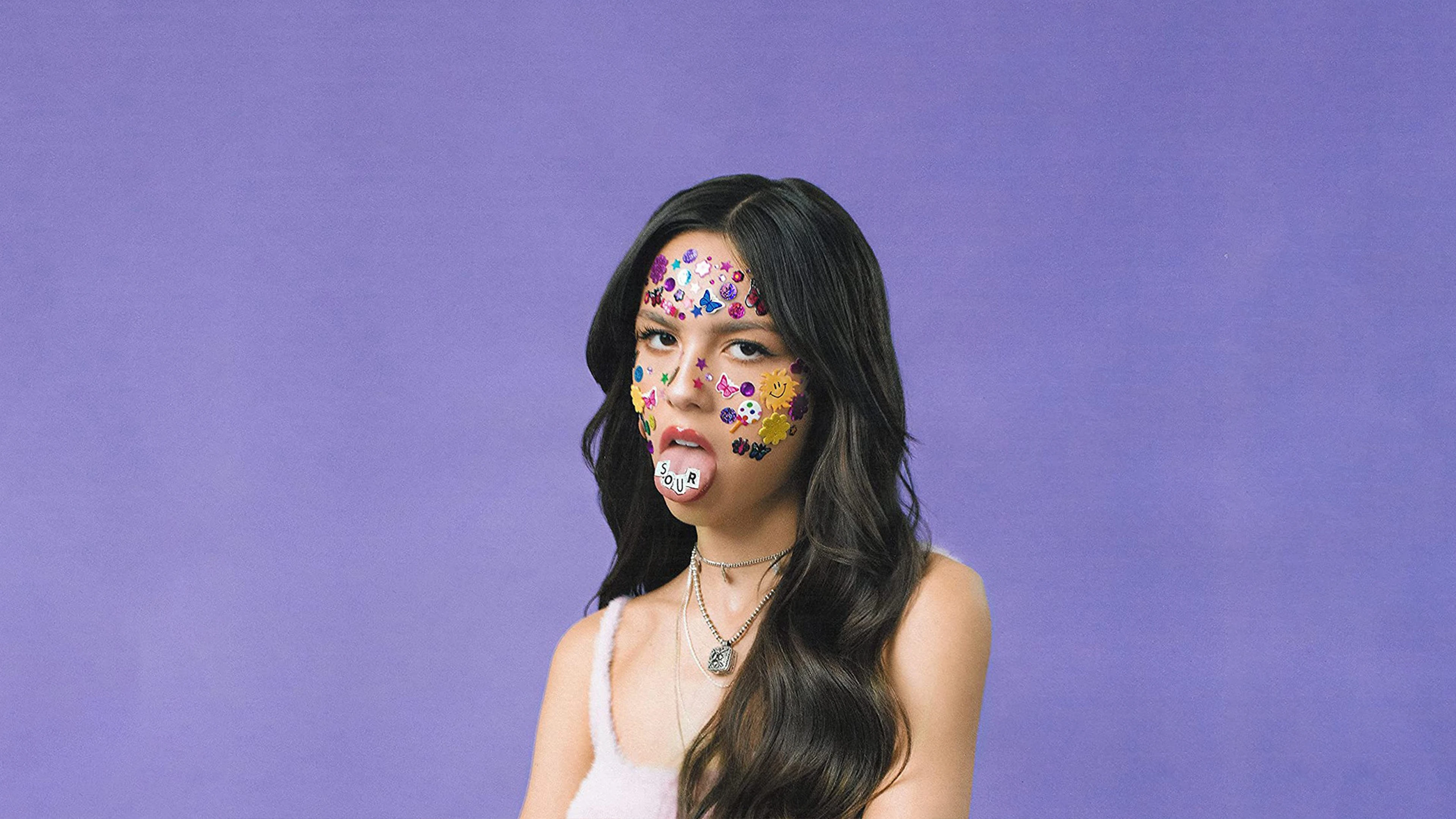 Person with face stickers against purple background, displaying "SOUR" on their tongue.