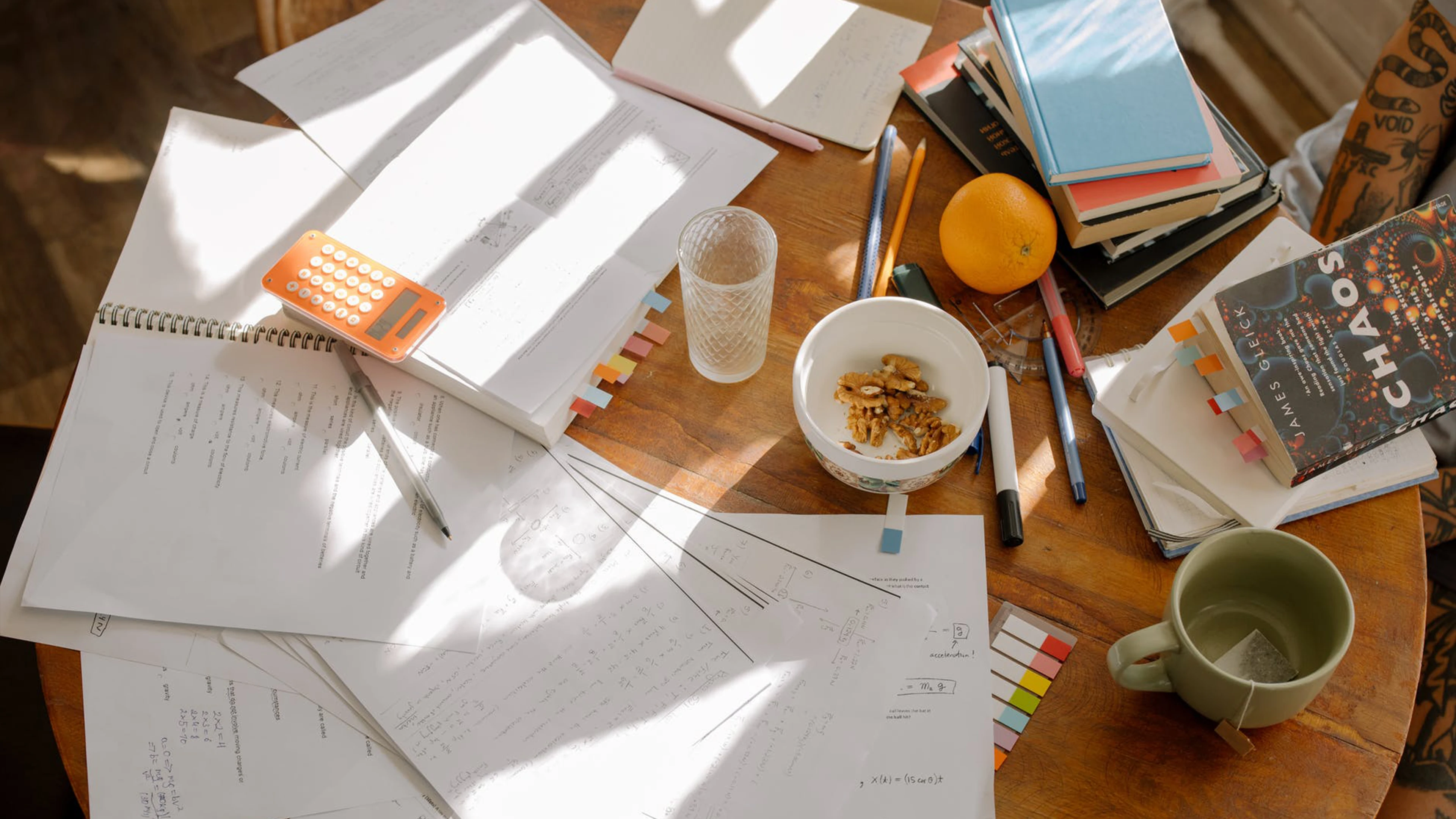 notebooks, papers, calculator, books, walnuts, tea, and an orange.