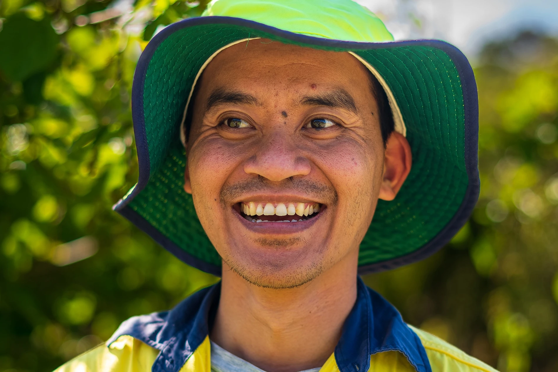 Green Connect Farm: Volunteer Photography 4 Smiling Person In Greenyellow Hat And Hivis Jacket With Blurred Nature Background.