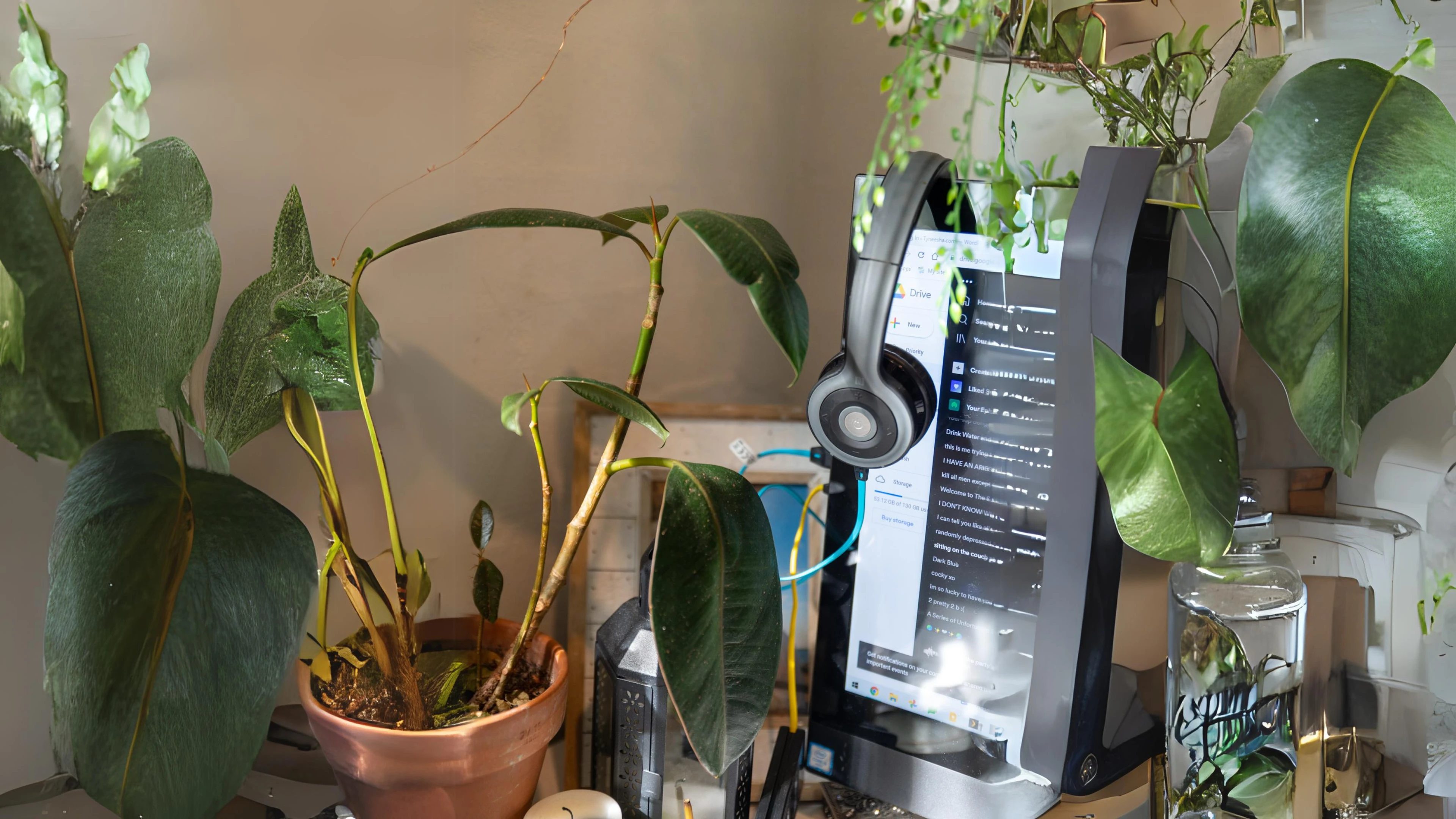 Computer monitor with headphones, surrounded by potted and hanging green plants on a desk.