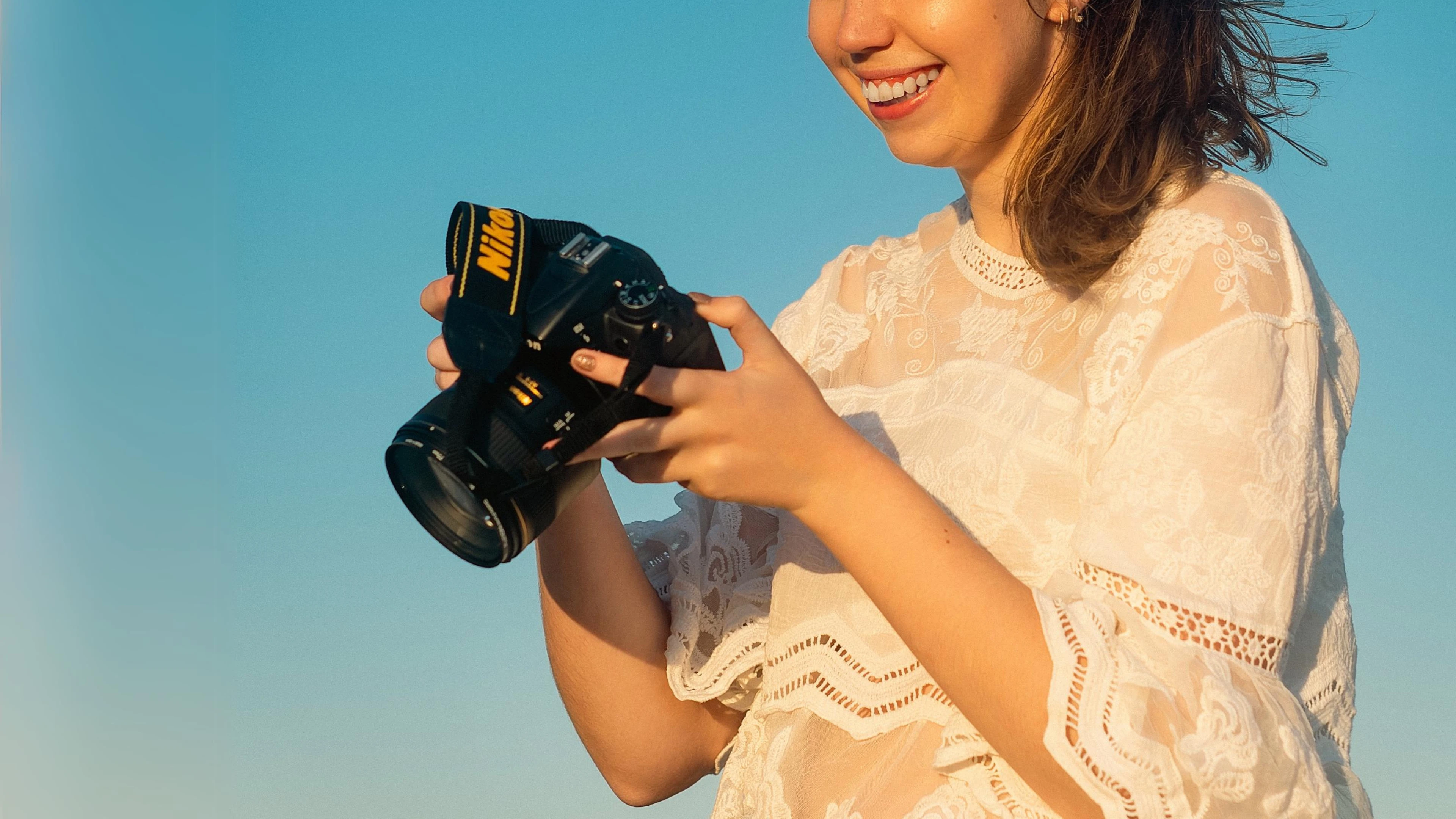 Person In Lacepatterned White Top Holding Nikon Camera Against Blue Sky.
