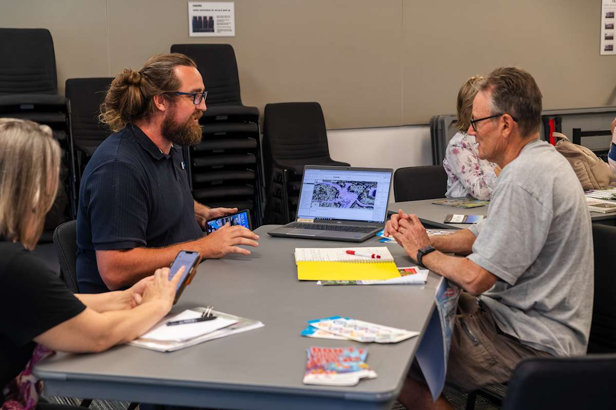 People in a meeting room using phones and a laptop with a map on the screen.