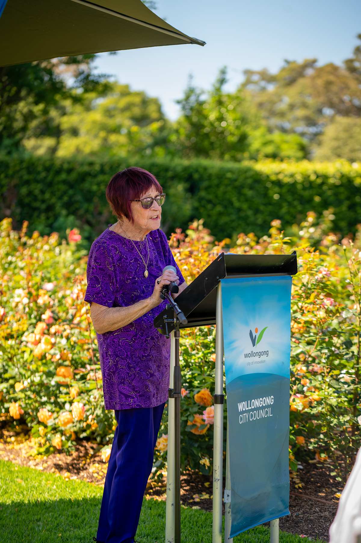Person delivering a speech at Wollongong City Council podium in a garden setting.