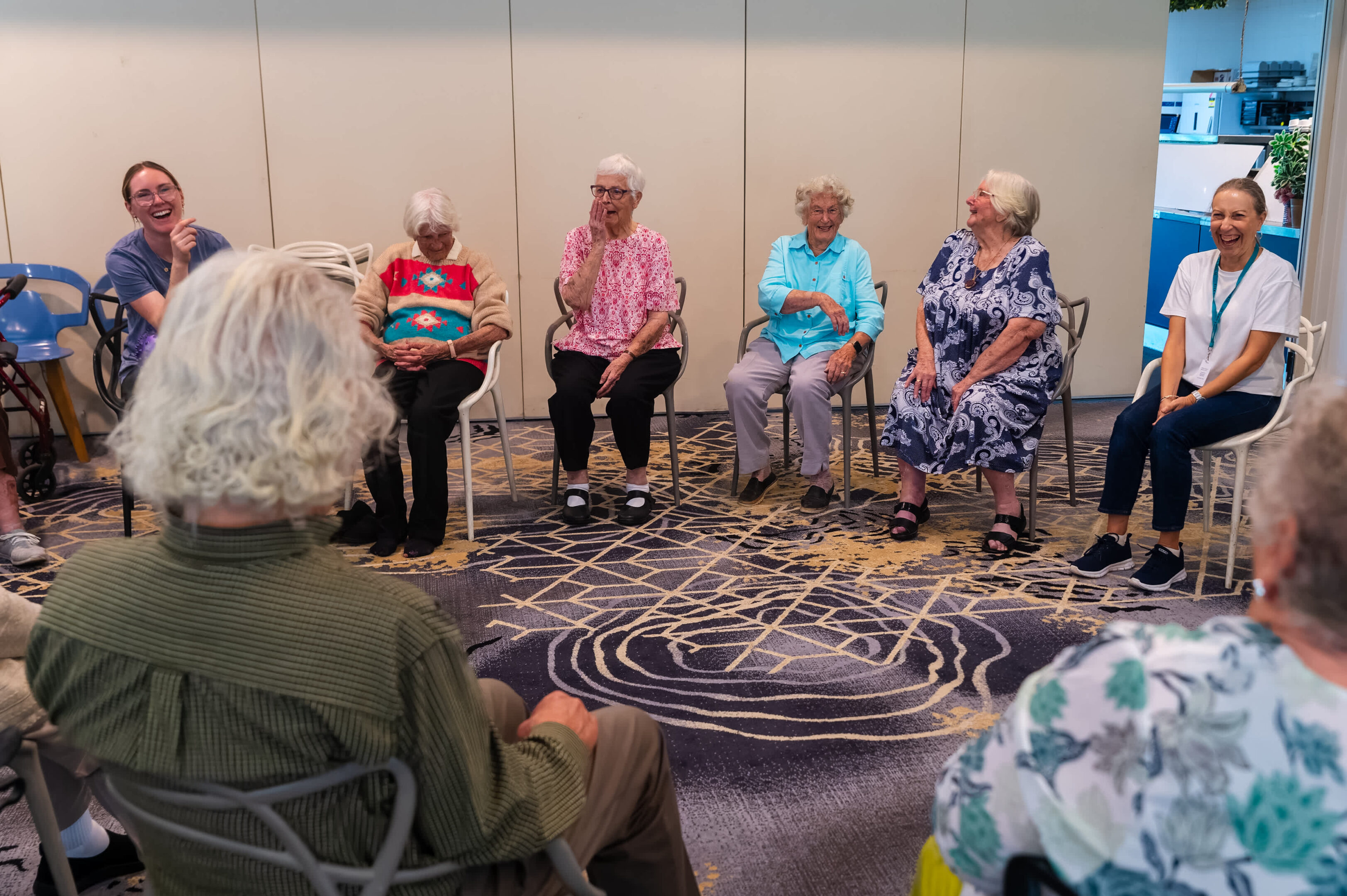 Great Reviews For Nina'S Cafe Club: 'One Of The Best Groups I’ve Joined In My Life' 1 Elders And A Young Person Seated Indoors, Conversing And Laughing In A Brightly Lit Room.