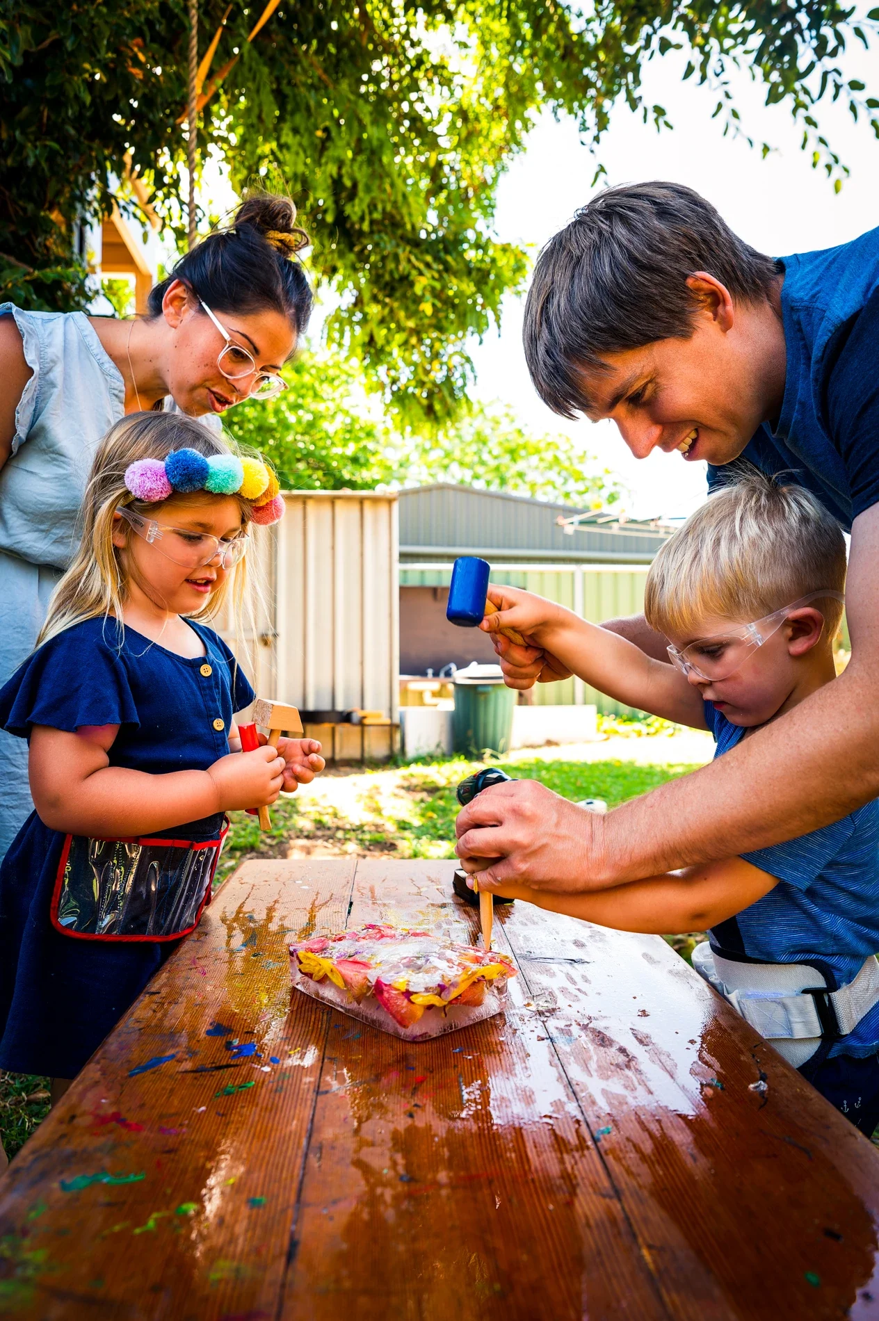 Why Lifestyle Family Photos Matter: Authentically Capturing Your Connections With Care 1 Family Doing Outdoor Ice Craft With Hammers In Sunny Backyard Setting.