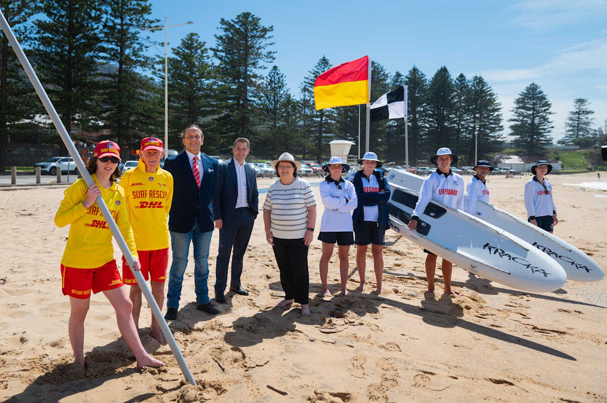 Group Of Surf Rescue Personnel, Lifeguards, And Officials Standing On A Beach With Rescue Boards And Flags.