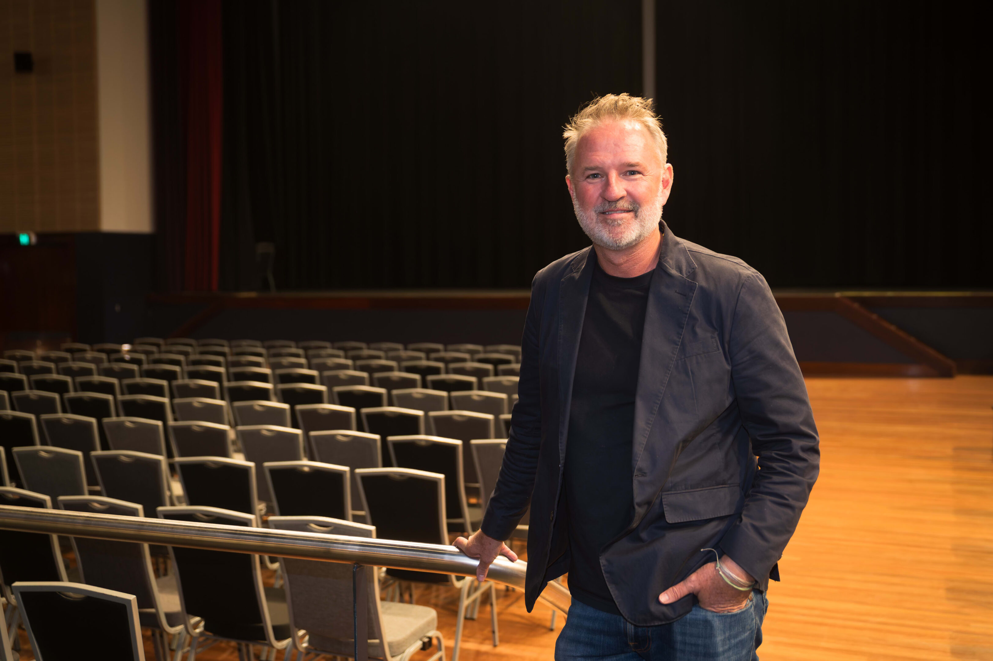 'Beautiful' Planet Wind Documentary Praised At Uow Screening 1 Man In Dark Jacket And Jeans Standing By Railing In Empty Auditorium With Chairs And Wooden Floor.